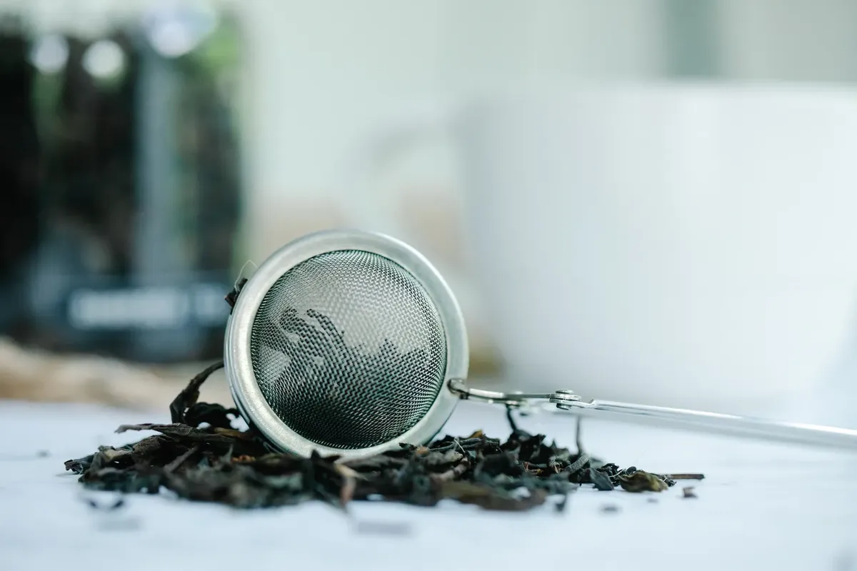 Metal tea infuser surrounded by loose tea leaves in a serene setting.