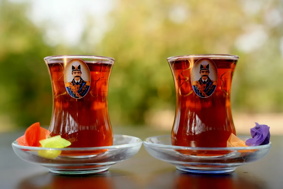 Two traditional Persian tea glasses with saucers against a blurred outdoor background, capturing the essence of classic tea culture.