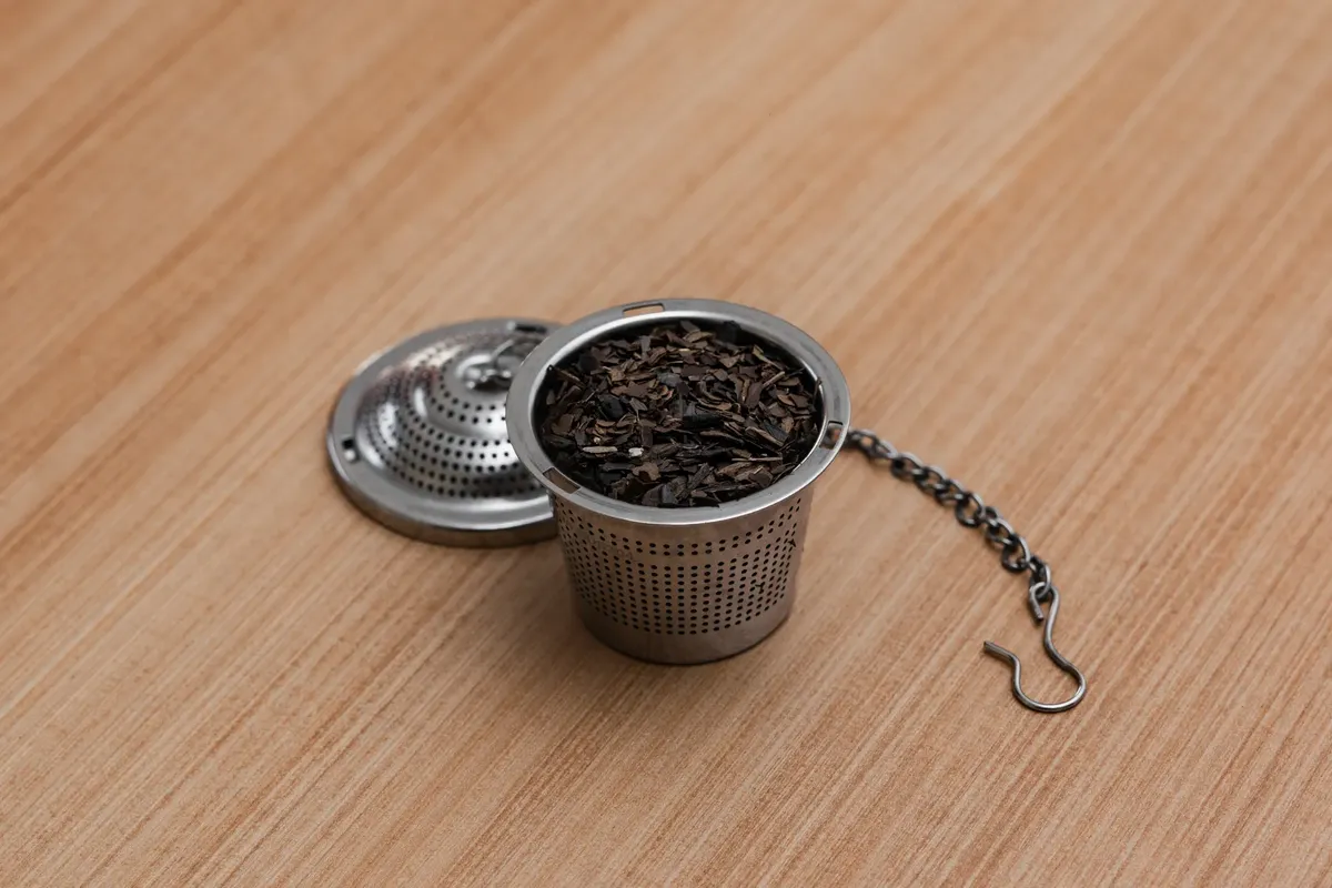 A stainless steel tea infuser containing loose leaf tea on a wooden surface.